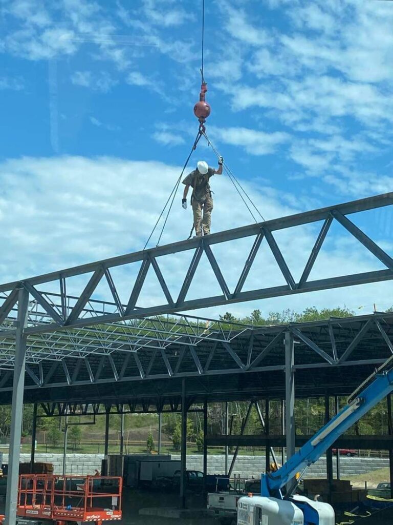 A man stands on a steel beam, expertly working on a steel erection project for a construction company.